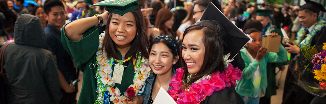 Three students at graduation, smiling. 